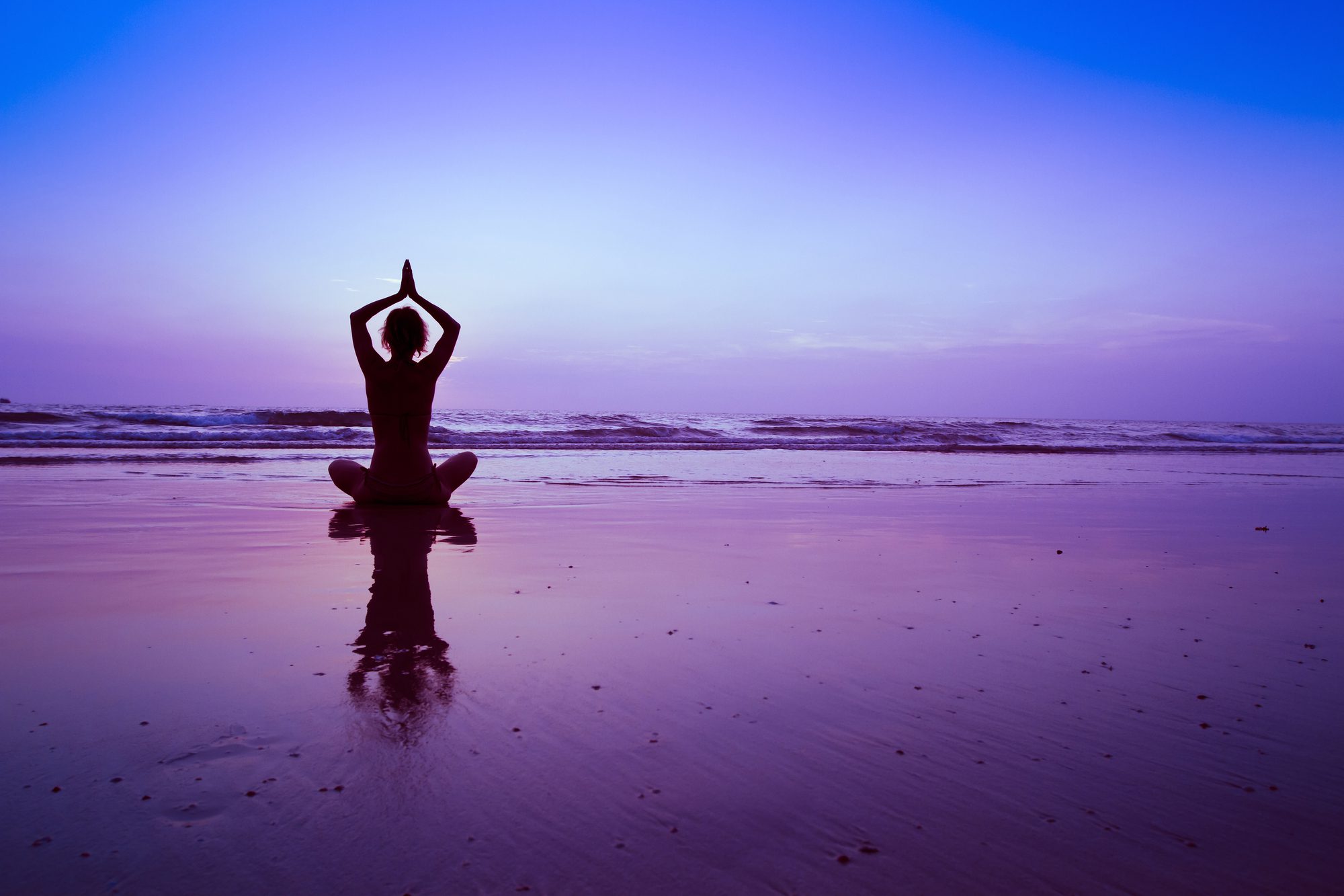 a woman practicing her chakra healing meditation on the beach