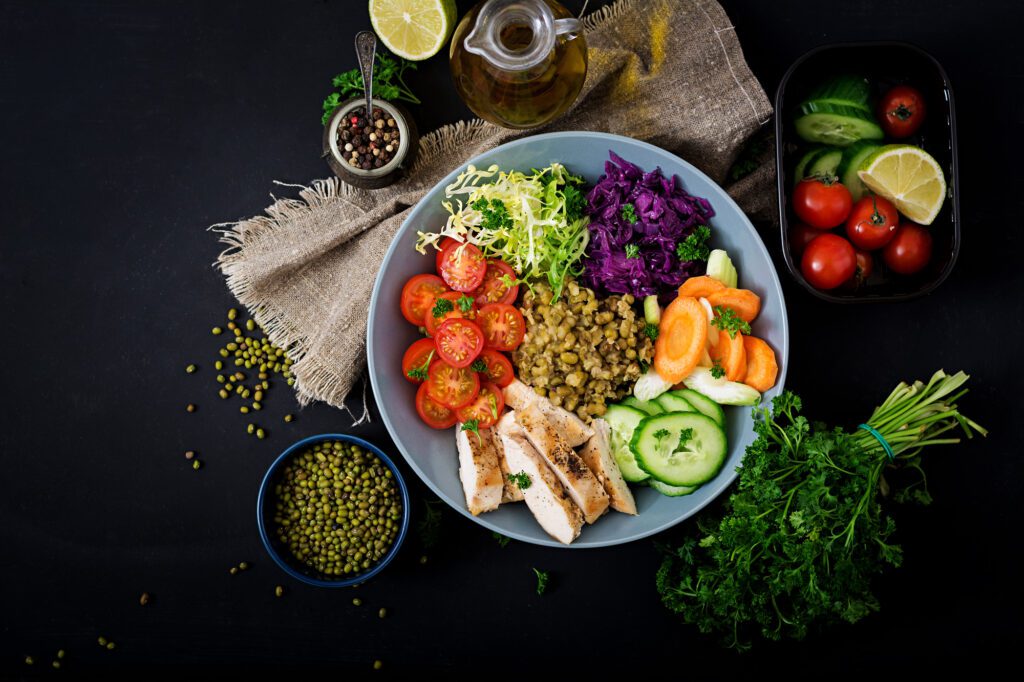 Healthy salad with chicken, tomatoes, cucumber, lettuce, carrot, celery, red cabbage and mung bean on dark background. Proper nutrition. Dietary menu. Flat lay. Top view